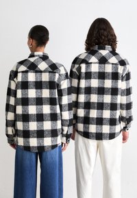 Tjekkede flannel skjorter i sort og hvid, med lange ærmer, knaplukkede manchetter og en afslappet pasform. Stoffet har en blød tekstur.