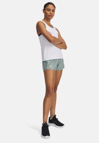 Baltas sportinis rankovių marškinėlis su juodu padu, derinamas su šviesiai žaliais šortais, turinčiais baltas apvadais, ir juodais sportiniais bateliais su tekstūruota paviršiumi.