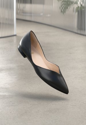 Chaussure plate en cuir noir avec un bout pointu et un petit talon brillant. L'intérieur présente une doublure beige clair. Design simple et épuré.