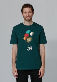 T-shirt en coton vert foncé avec un graphique d'astronaute tenant des ballons de planètes colorées dans différentes teintes et textures.