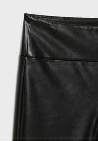 Gros plan sur une jupe en similicuir noire taille haute montrant une texture lisse et un détail de ceinture cousue.