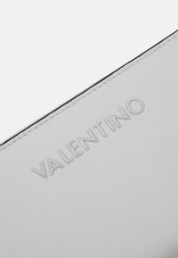 Cartera de piel blanca con logotipo "VALENTINO" en relieve, costuras visibles y una textura suave. Presenta un diseño limpio y minimalista.