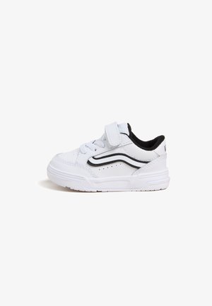 Biały sneaker dla malucha z czarnym falistym paskiem, zapinany na rzep, z sznurówkami i teksturowaną podeszwą na białym tle.