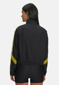 Zwarte windbreakerjas met gele zijstrepen, elastische zoom en een staande kraag. Soepele stof met een lichtgewicht ontwerp.