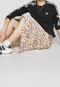 Svart långärmad topp med vita ränder, tillsammans med en krämfärgad kjol med bruna leopardfläckar. Svart och vit sportskor.