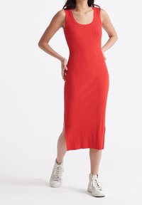 Punainen ribbikuvioinen midimekko, jossa on pyöreä kaula-aukko ja sivuhalkiot. Yhdistetty valkoisiin korkeakorkoisiin tennareihin.