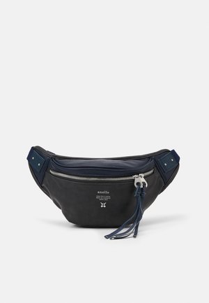 Sac banane en tissu noir avec une fermeture éclair métallique, des accents bleu marine et une bandoulière réglable. Présente un imprimé logo et des pompons décoratifs.
