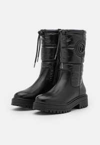 Botas negras hasta la rodilla con una parte inferior de cuero brillante y una parte superior de nylon acolchado. Presentan un cierre de toggles y un acento de logo circular.