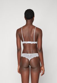 Weißes Spitzen-Bra- und Slip-Set, mit dünnen Trägern, zarter Spitzenbordüre und Blumenmustern, von hinten betrachtet. Glatte Textur.