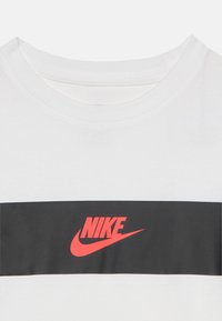 Weißes T-Shirt mit rundem Ausschnitt. Verfügt über einen horizontalen schwarzen Streifen mit einem roten Nike-Logo in der Mitte. Baumwollmaterial.