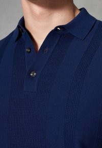 Polo en maille bleu marine avec des motifs en côtes, deux boutons et un col classique en tissu texturé.