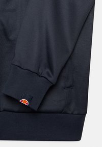 Felpa blu navy in tessuto con polsini e orlo a costine. Presenta una piccola etichetta con un design arancione e bianco. Texture liscia.