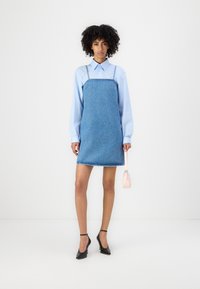 Denimmekko, jossa on ohuet olkaimet, vaaleansininen paita alla ja vaaleanpunainen käsilaukku. Mustat korkokengät viimeistelevät asun. Yksinkertainen helman muoto.