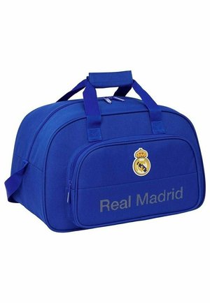 Niebieska torba sportowa z logo i napisem Real Madrid, podwójne uchwyty, przednia kieszeń na zamek i boczny pasek.
