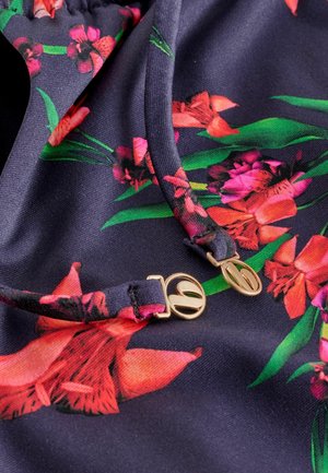 Ziedu raksta audums tumši zilā krāsā ar košām sarkanām un rozā ziedēm un zaļām lapām. Zelta detaļas pie regulējamām plecu siksnām.