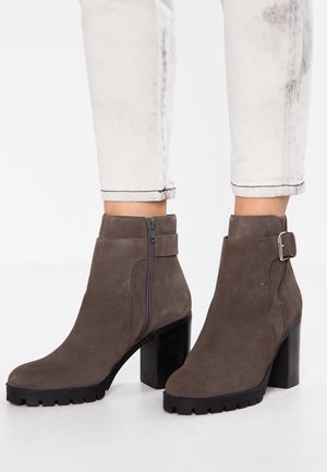 Zamszowe botki za kostkę w kolorze szarym z masywnym czarnym obcasem, bocznym zamkiem błyskawicznym i detalem w postaci paska z srebrną klamrą. Teksturowana gumowa podeszwa.