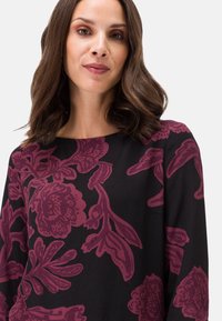 Top nero con un design floreale in un profondo bordeaux, maniche lunghe e scollo rotondo. Tessuto liscio e fit comodo.