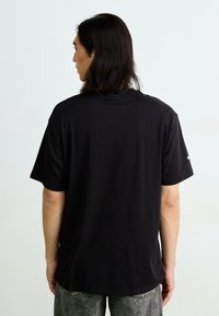 Sort t-shirt med afslappet pasform, korte ærmer og rund hals. Har subtil logoaccent på ærmet. Glat bomuldsstruktur.