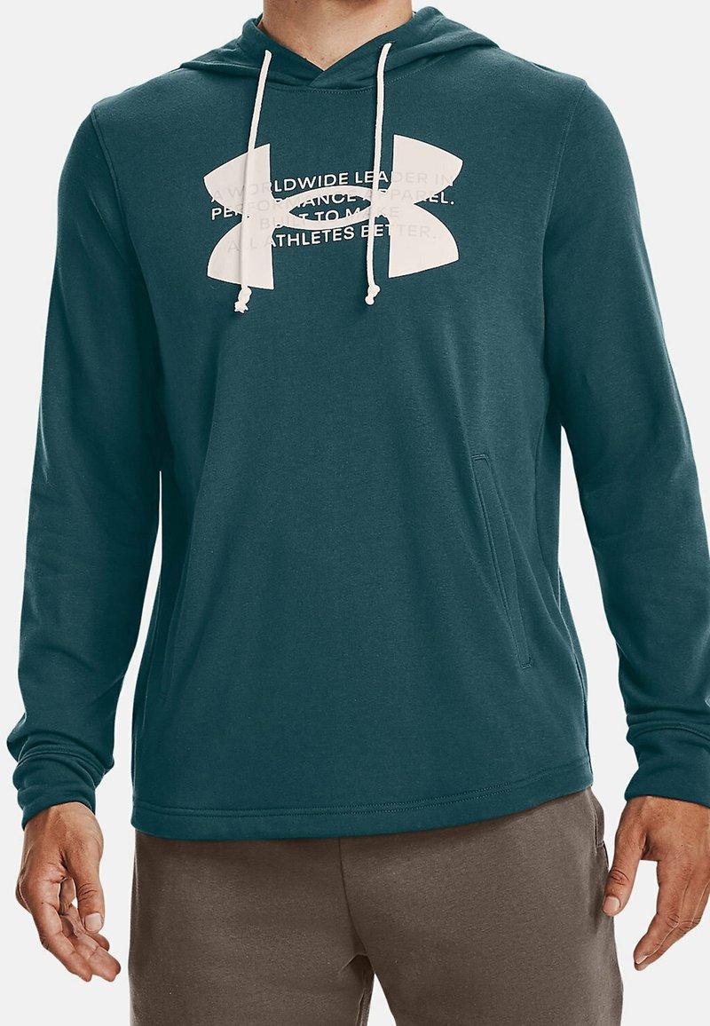 Homme portant un sweat à capuche bleu sarcelle foncé avec un grand logo blanc Under Armour et des cordons blancs.