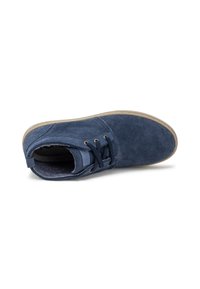 Botín de ante azul marino con suela de goma beige, puntera redonda y cordones oscuros. Presenta un suave forro interior y un diseño minimalista.