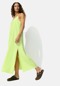 Robe maxi vert clair avec fentes sur les côtés, en tissu doux. Associée à des chaussures à enfiler marron foncé avec des accents cloutés.