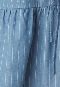 Zils denims audums ar baltām vertikālām svītrām, kas izceļas ar savilkuma detalizāciju un aukliņu. Mīksta tekstūra, vidēja svara, ikdienišķs dizains.