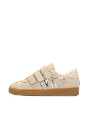 Beige suède sneaker met drie klittenbandsluitingen, zilverkleurig decoratief detail aan de zijkant en een bruine rubberen zool.