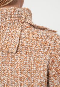 Tkan prepleto pulover z velikim ovratnikom, v kombinaciji oranžne in krem barve, z rebrastim vzorcem in vidnimi šivi.