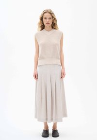Stickad ärmlös topp i ljusbeige, kombinerad med en lång, plisserad beige kjol. Svarta platta skor fulländar outfitten. Svala texturer, enkel design.