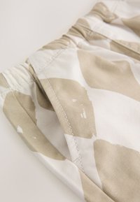 Tissu beige clair avec de grandes formes taupe irrégulières ; doté d'une taille élastique et de coutures visibles. Texture lisse.