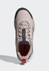 Beige athletic shoe with a mesh upper, gray accents, and contrasting dark toe cap. Includes a red heel loop and sturdy laces.