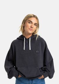 Donkergrijze oversized hoodie van zachte stof. Beschikt over een capuchon met trekkoord, een voorkant zak en een klein logo op de borst. Witte trekkoorden.