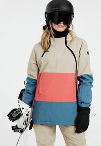 Skijacke in Beige, Koralle und Türkis; wasserdichtes Gewebe, verstellbare Kapuze, Reißverschlussdetails, kombiniert mit einem Snowboard und einem schwarzen Helm.
