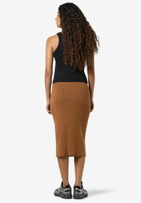 Un débardeur noir, une jupe midi marron côtelée et des baskets grises. La tenue présente un design ajusté et un tissu texturé dans une couleur chaude.