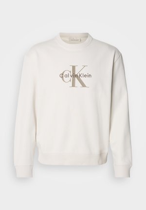 Hvid crewneck sweatshirt lavet af blødt stof, der har et stort beige Calvin Klein-logo på forsiden, med ribbede manchetter og bund.