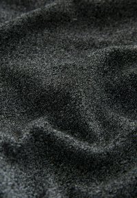 Schwarzer strukturierter Stoff mit einer weichen, leicht rauen Oberfläche. Das Material zeigt subtile Farbnuancen und erzeugt eine reiche visuelle Tiefe.