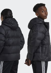 Black puffer jacket with a hood, featuring a quilted design and side zipper pockets. Smooth texture and lightweight insulation.