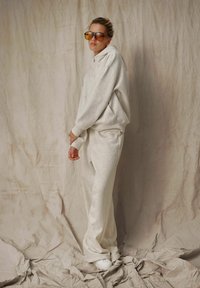 Jasnoszara bluza z kapturem oraz dopasowane spodnie dresowe z miękkiego materiału. Bluza ma luźny krój, podczas gdy spodnie cechują się prostym krojem.