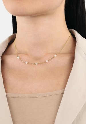 Collar de cadena de oro con perlas blancas pequeñas espaciadas uniformemente, con elementos entrelazados que crean un diseño elegante. Lleva puesto sobre piel desnuda.