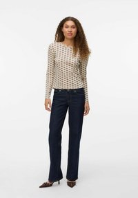 Blusa de manga larga color crema con un patrón repetido, combinada con unos jeans rectos de pierna oscura y unos zapatos de tacón altos marrones.