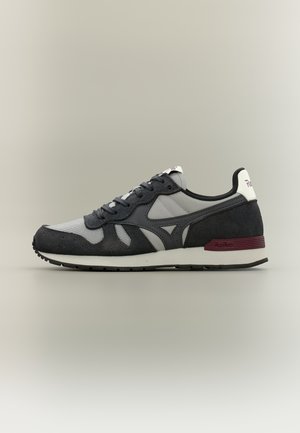 Αθλητικό παπούτσι σε μαύρο και γκρι με λευκή σόλα και λεπτομέρεια μπορντό στη φτέρνα, σε πλευρική όψη πάνω σε ουδέτερο φόντο.