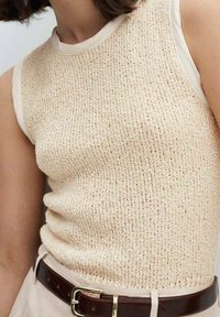 Skrócony bezrękawnik w jasnym beżu z teksturowanej tkaniny, z okrągłym dekoltem i kontrastującymi kremowymi wykończeniami. Brązowy pasek akcentujący w talii.