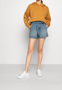 Hnědá mikina s kapucí, světle modré džínové šortky se zavazováním v pase a bílé tenisky. Šortky jsou přiléhavé a srolovanými lemy. Jednoduchý a ležérní vzhled.