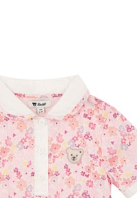 Polo rosa con motivo floreale e colletto bianco, caratterizzato da un patch di un orso sul lato sinistro e chiusura frontale con tre bottoni.