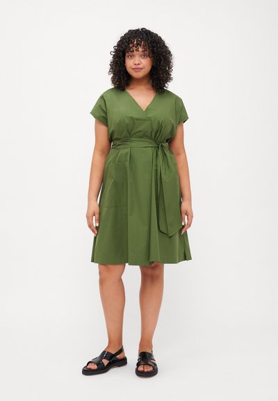 Abito verde al ginocchio con scollatura a V, maniche corte e vita con cintura. Realizzato in tessuto liscio con due tasche laterali. Sandali neri.