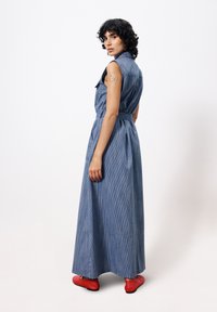 Denim-Maxikleid mit vertikalen Streifen, ärmellosem Design, gebundenem Taillenbund und lockerer Passform, kombiniert mit roten Schuhen.