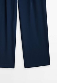 Pantalon large bleu marine en tissu lisse, présentant une coupe ajustée et des lignes épurées sans éléments apparents ni motifs.