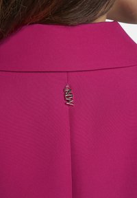 Fuchsia-pinkes Kleidungsstück mit glatter Textur und einem Kragen. Verfügt über ein silbernes Logo-Tag am Hinterhals für Details.