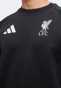 Μαύρο αθλητικό μπλουζάκι με λευκό λογότυπο Adidas αριστερά και έμβλημα της Liverpool Football Club δεξιά στο στήθος.