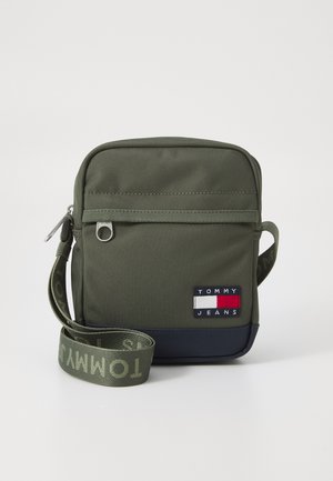 Green fabric crossbody bag with a zip closure, featuring a navy bottom, logo patch, and a patterned strap reading “TOMMY.”